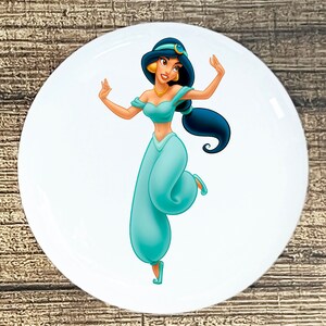 May include: A white round sticker with a cartoon image of a woman with long black hair wearing a blue and green outfit. She is dancing with her arms raised.