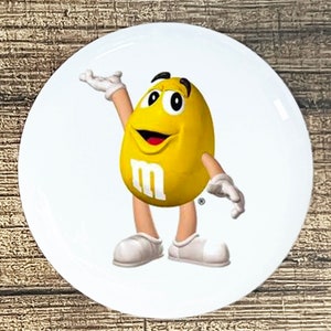 May include: A yellow M&M's character with a big smile and outstretched arms, standing on a white background.