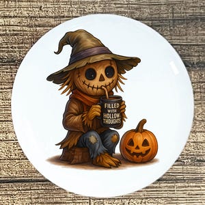 May include: A white ceramic plate featuring a Halloween-themed illustration. The image depicts a scarecrow figure with a stitched mouth, wearing a hat and holding a mug that reads "FILLED WITH HOLLOW THOUGHTS." A carved pumpkin sits nearby.