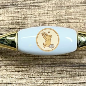 May include: A white ceramic cabinet knob with a gold metal base. The knob features a Winnie the Pooh illustration.