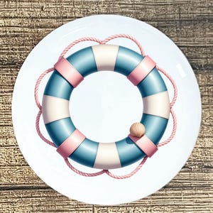 May include: A round white plate featuring a nautical design. The design includes a blue, white, and pink life preserver with a rope and a small seashell. The plate is on a wooden surface.