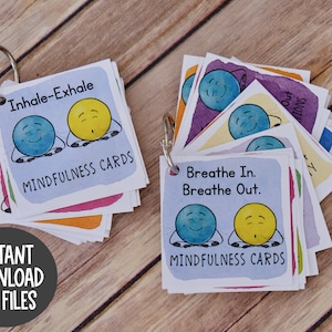Puede incluir: Un juego de tarjetas de atenci&oacute;n plena de colores con ilustraciones de dos caras de dibujos animados. Las tarjetas est&aacute;n unidas con un anillo plateado. El texto en las tarjetas dice "Inhala-Exhala" y "Inhala. Exhala." Las tarjetas est&aacute;n etiquetadas como "Tarjetas de atenci&oacute;n plena".