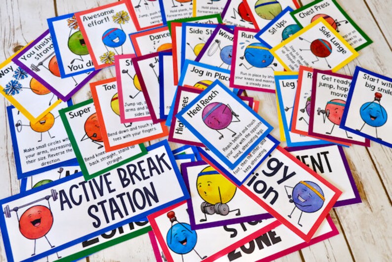 May include: A colorful set of activity cards featuring cartoon characters with different exercise poses. The cards are labeled with exercise names like "Heel Reach", "Side Stretch", and "Sit Ups". The cards are arranged on a white wooden surface with a larger card in the foreground that reads "Active Break Station".