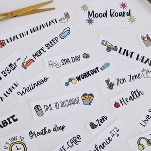 May include: A selection of white rectangular stickers with black text and colourful illustrations related to health and wellbeing. Phrases include "Healthy Breakfast," "More Sleep," "Workout," and "Live Healthy." Gold scissors are in the upper left.