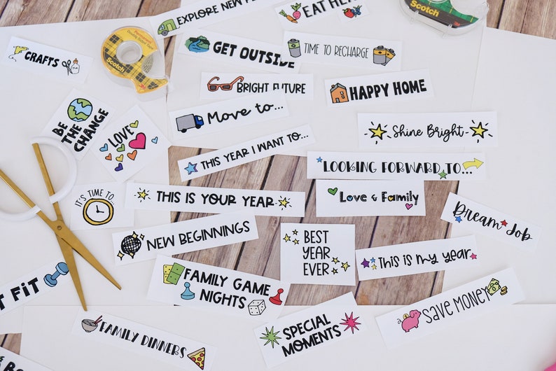 May include: A selection of white rectangular stickers featuring phrases and illustrations such as "Crafts," "Get Outside," "Happy Home," and "Save Money." Gold scissors and a roll of Scotch tape are also visible.