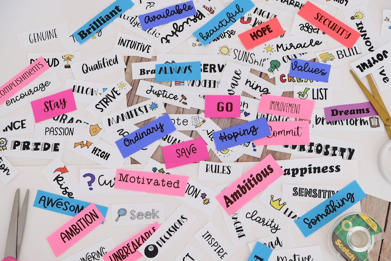 May include: A selection of white rectangular stickers with words and phrases such as "Ambition", "Hope", and "Dreams" in black ink. Some stickers are pink and blue. Scissors and tape are also visible.