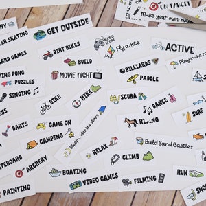 May include: A selection of activity labels on white paper, including "Photography," "Roller Skating," and "Get Outside." Pink scissors are on the paper. The labels feature hand-drawn illustrations and black text.