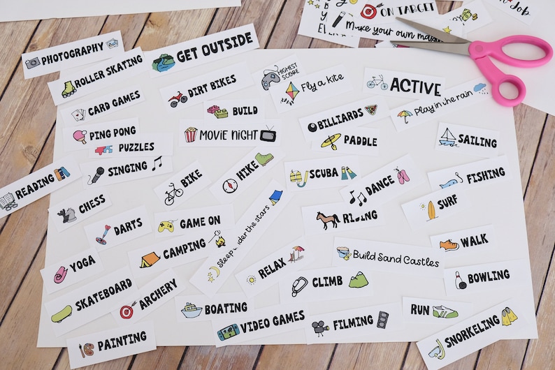 May include: A selection of activity labels on white paper, including "Photography," "Roller Skating," and "Get Outside." Pink scissors are on the paper. The labels feature hand-drawn illustrations and black text.