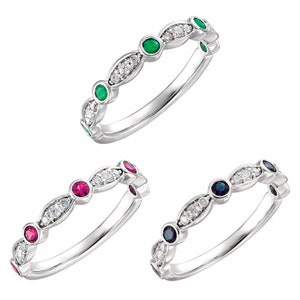 May include: Three silver rings with a row of small diamonds and a larger gemstone in the center. The rings feature different colored gemstones: green, red, and blue.
