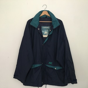 May include: A navy blue jacket with a green lining and a zipper closure. The jacket has a pocket on the front with the Helly Hansen logo.