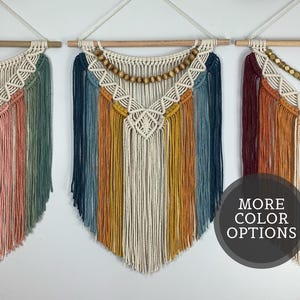 Pode incluir: Tr&ecirc;s tape&ccedil;arias de macram&eacute; penduradas em var&otilde;es de madeira. Cada pe&ccedil;a apresenta padr&otilde;es de n&oacute;s intrincados, franjas longas e contas de madeira. Os designs incorporam v&aacute;rias paletas de cores, incluindo rosa, verde, azul, amarelo e vermelho escuro.