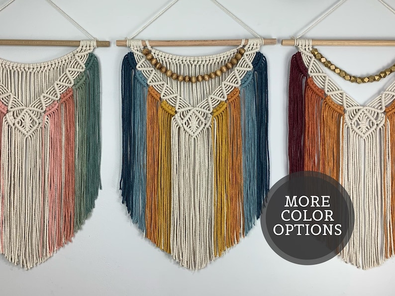Pode incluir: Tr&ecirc;s tape&ccedil;arias de macram&eacute; penduradas em var&otilde;es de madeira. Cada pe&ccedil;a apresenta padr&otilde;es de n&oacute;s intrincados, franjas longas e contas de madeira. Os designs incorporam v&aacute;rias paletas de cores, incluindo rosa, verde, azul, amarelo e vermelho escuro.