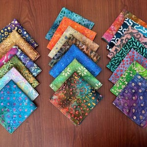 May include: A collection of 24 colorful fabric squares with various patterns, including floral, geometric, and abstract designs. The squares are arranged in two rows of 12, with each row featuring a different color scheme.