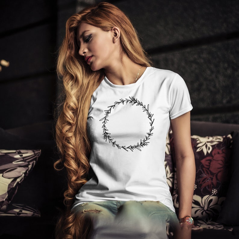 K&ouml;nnte beinhalten: Ein wei&szlig;es T-Shirt mit einem schwarzen floralen Kranzdesign. Der Kranz ist ein Kreis aus Bl&auml;ttern und Zweigen.