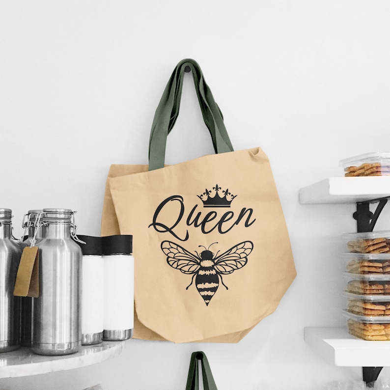 May include: A beige tote bag with green handles and a black bee with a crown and the word "Queen" printed on it.