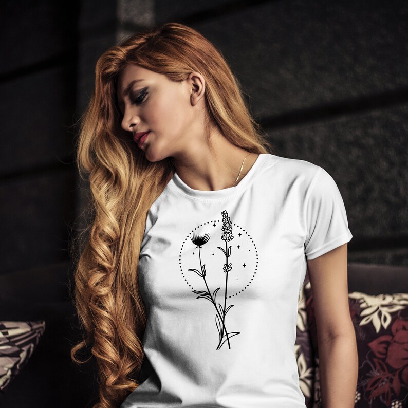 May include: White t-shirt featuring a black floral design with a circle of stars. The design includes a dandelion and lavender sprig. The shirt has short sleeves and a crew neck.