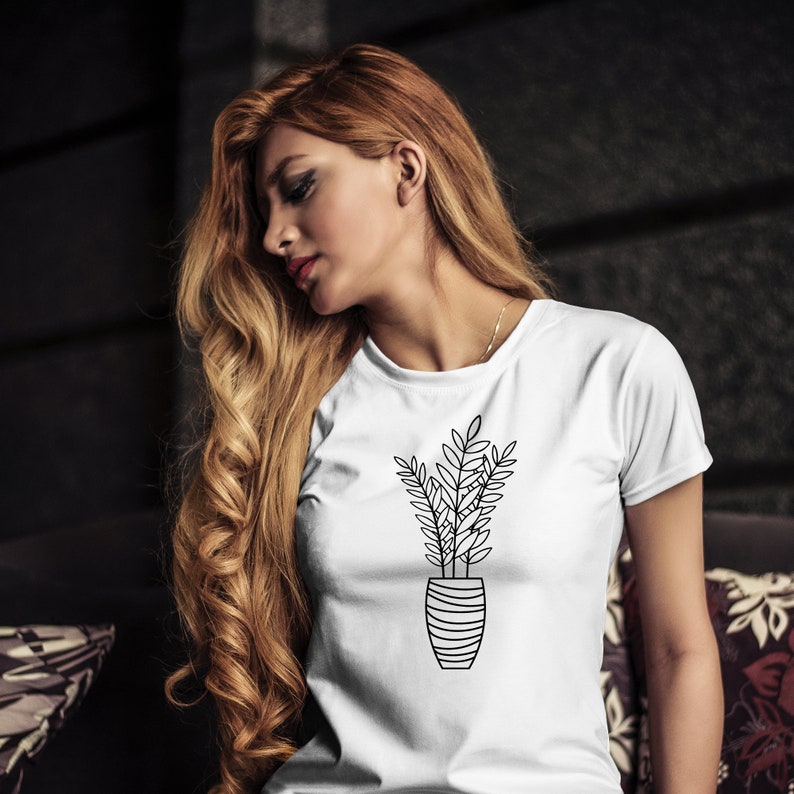 May include: White t-shirt with a black line drawing of a potted plant. The plant has long, thin leaves and is in a striped pot.