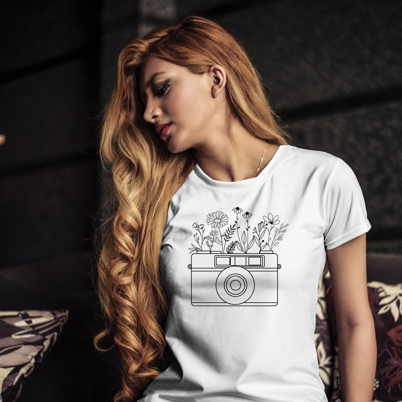 K&ouml;nnte beinhalten: Wei&szlig;es T-Shirt mit einer schwarzen Linienzeichnung einer Kamera, aus der Blumen wachsen.