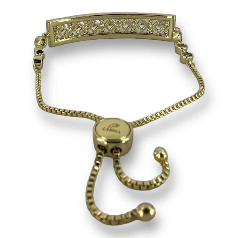 May include: Gold-toned bracelet with a rectangular centerpiece featuring a geometric design. The bracelet has a delicate chain and an adjustable sliding clasp. The word "CHINA" is visible on the clasp.