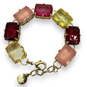 Puede incluir: Un brazalete de cadena dorada con ocho piedras rectangulares facetadas en tonos de rosa, amarillo y rojo. El brazalete tiene un cierre de mosquetón y una pequeña etiqueta con el texto "CHARLOTTE RUSSE" en ella.