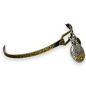 May include: A hammered brass-tone bangle bracelet with a silver-tone charm. The charm is heart-shaped with the word "Fearless" in script and gold accents. The bracelet has a hook closure.