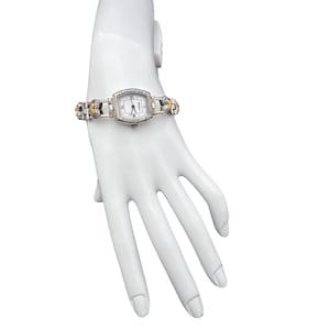 May include: Silver-toned rectangular watch with a white face and Roman numeral hour markers. The watch band features silver and gold-toned accents. The watch is displayed on a white mannequin hand.