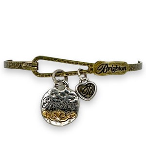 May include: A gold-toned metal bracelet with a safety pin clasp. The bracelet features two charms: a silver-toned oval charm with the word "Fearless" and a gold-toned heart charm with a "B" design. The word "Brighton" is engraved on the bracelet.