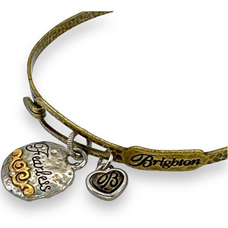 May include: A gold-toned metal bangle bracelet with three charms. One charm is a silver-toned heart with a 'B' in the center. Another is a silver-toned disc with the word 'Fearless' and gold accents. The bracelet is marked 'Brighton'.
