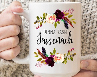 May include: White ceramic mug with a floral design in shades of burgundy, pink, and green. The mug has the text "Dinna Fash Sassenach" printed on it.