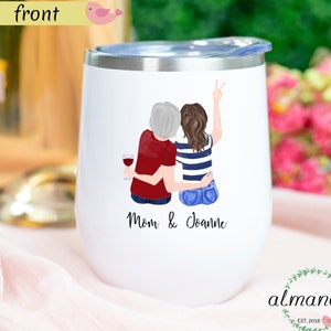 May include: White insulated wine tumbler with a silver rim and lid. The tumbler features a graphic of two figures embracing, one holding a wine glass. The text "Mom & Joanne" is printed below the graphic. The brand logo is at the bottom.