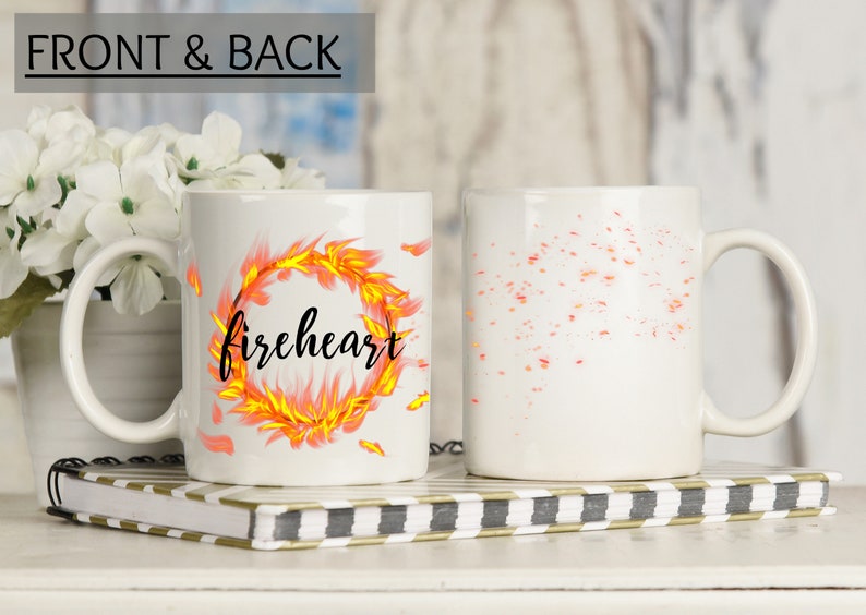 Puede incluir: Taza de cer&aacute;mica blanca con un dise&ntilde;o negro y naranja. El dise&ntilde;o presenta un anillo de fuego con la palabra "fireheart" escrita en su interior. La parte posterior de la taza tiene un dise&ntilde;o naranja y amarillo disperso.
