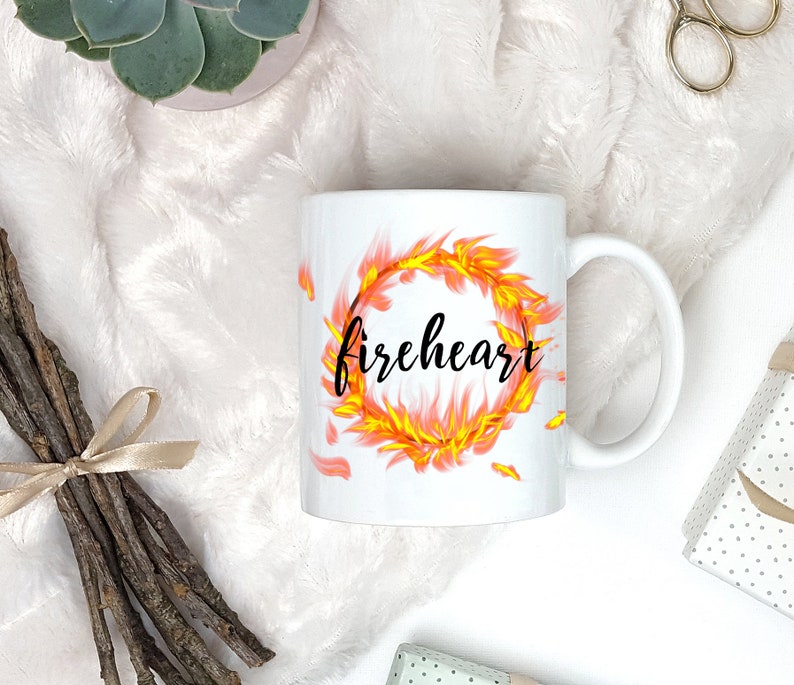Puede incluir: Taza de cer&aacute;mica blanca con un dise&ntilde;o de fuego negro y amarillo y la palabra "fireheart" en letras negras.