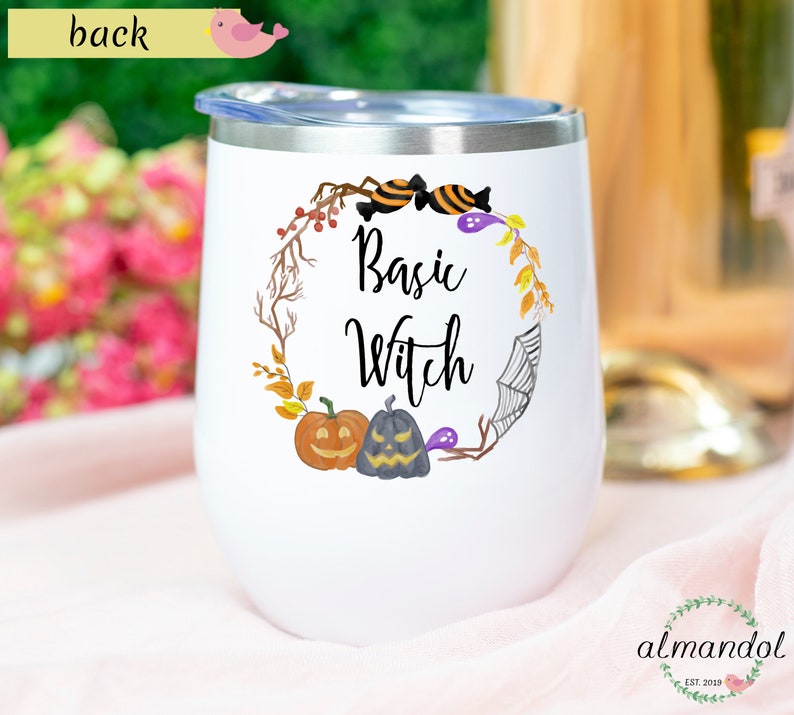 May include: White stainless steel wine tumbler with a purple and black design featuring a wreath of fall leaves, pumpkins, candy, and a spider web. The text "Basic Witch" is in the center of the design.