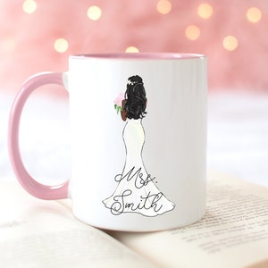 Pu&ograve; includere: Tazza in ceramica bianca con bordo e manico rosa. La tazza presenta un'illustrazione in bianco e nero di una sposa in abito da sposa che tiene un mazzo di fiori. Il testo "Mrs. Smith" &egrave; scritto sotto l'illustrazione.