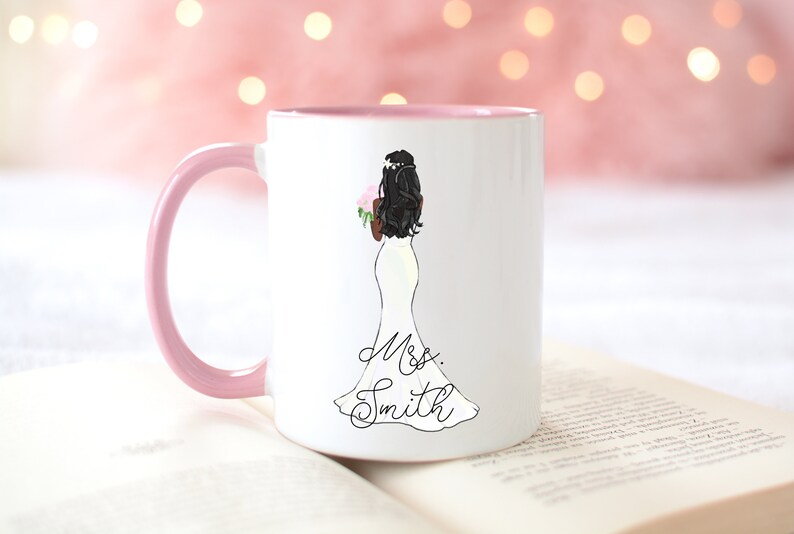 Pu&ograve; includere: Tazza in ceramica bianca con bordo e manico rosa. La tazza presenta un'illustrazione in bianco e nero di una sposa in abito da sposa che tiene un mazzo di fiori. Il testo "Mrs. Smith" &egrave; scritto sotto l'illustrazione.