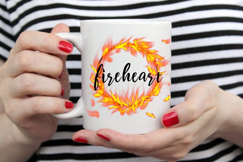 Puede incluir: Taza de cer&aacute;mica blanca con un dise&ntilde;o de fuego y la palabra "fireheart" en letras negras.