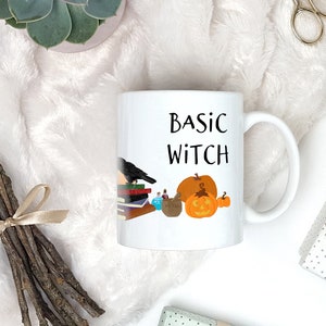 Pode incluir: Caneca de cer&acirc;mica branca com al&ccedil;a preta. A caneca tem um gr&aacute;fico preto de um corvo, livros, garrafas de po&ccedil;&otilde;es e uma ab&oacute;bora. O texto "BASIC WITCH" &eacute; impresso em preto na caneca.