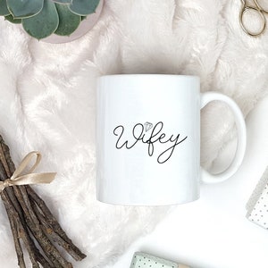Pu&ograve; includere: Tazza in ceramica bianca con una scritta in corsivo nero che recita "wifey" con un piccolo grafico di diamante sopra la parola.