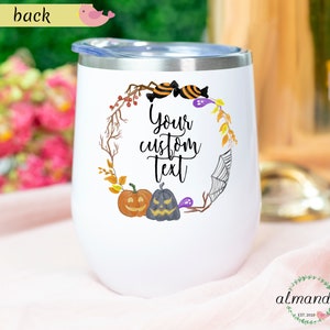 May include: White stainless steel wine tumbler with a Halloween themed design. The design features a wreath with pumpkins, candy corn, and a spider web. The text "Your custom text" is in the center of the wreath.