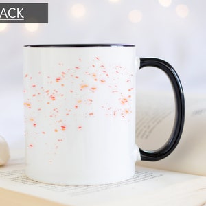Puede incluir: Taza de cer&aacute;mica blanca con borde y asa negros. La taza tiene un dise&ntilde;o de puntos naranja y rojo dispersos en la parte delantera.