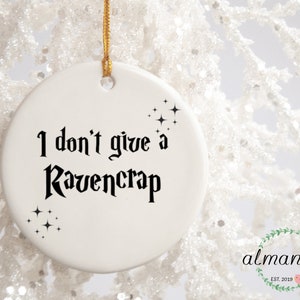May include: White ceramic Christmas ornament with black text that reads "I don't give a Ravencrap" and black star-shaped sparkles.