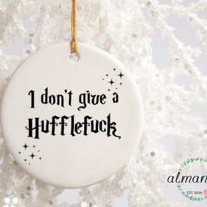 May include: White ceramic Christmas ornament with black text that reads "I don't give a Hufflefuck" with small black stars around the text.