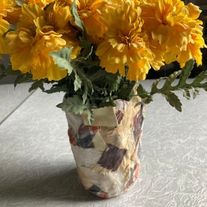 May include: A bouquet of bright yellow marigolds in a patchwork fabric vase.