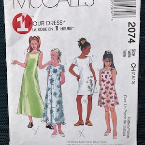May include: McCall's sewing pattern featuring four dress designs for girls. The pattern includes a green dress, a blue floral dress, a white dress with floral accents, and a pink butterfly dress. The text reads "1 Hour Dress".