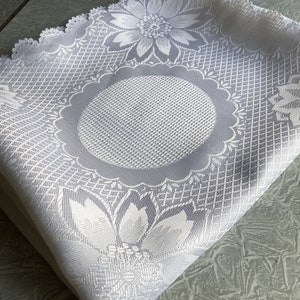 May include: White lace tablecloth with a scalloped edge and a floral design. The tablecloth has a large, circular design in the center.