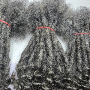 Op de afbeelding: Drie bundels grijze, krullende, synthetische dreadlocks met rode elastiekjes.