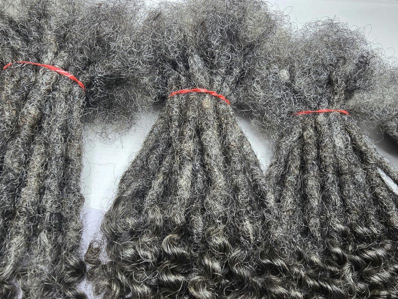 Op de afbeelding: Drie bundels grijze, krullende, synthetische dreadlocks met rode elastiekjes.