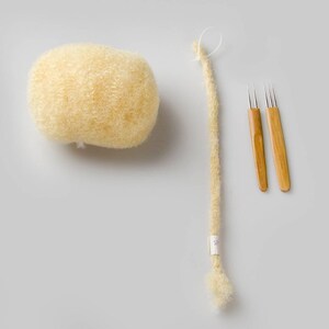 May include: A ball of light brown wool yarn, a long strand of light brown yarn, and two wooden crochet needles.
