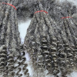 Op de afbeelding: Een bundel grijze, krullende synthetische dreadlocks. De dreadlocks zijn lang en dik en hebben een natuurlijke, textuurrijke uitstraling.