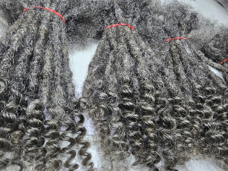 Op de afbeelding: Een bundel grijze, krullende synthetische dreadlocks. De dreadlocks zijn lang en dik en hebben een natuurlijke, textuurrijke uitstraling.
